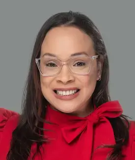 Woman with long, dark hair and glasses wearing a red blouse with a bow around her neck.