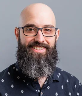 A photo of Chris DeLuca, a bald white man with a large beard, wearing glasses.