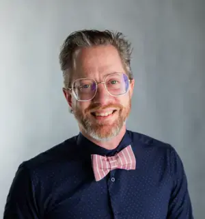 James Sansbury smiling, sporting a pink bowtie and nerdy glasses.