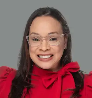 Woman with long, dark hair and glasses wearing a red blouse with a bow around her neck.
