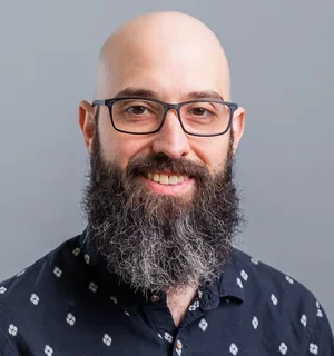 A photo of Chris DeLuca, a bald white man with a large beard, wearing glasses.