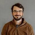 Javier Reartes wearing a brown hoodie in front of a gray background.