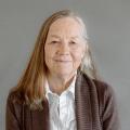 Karen Stevenson wearing a white button down shirt and blazer with gray backdrop behind her.