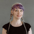 Pauline Judge wearing a short-sleeved black shirt and braided pigtails with purple hair in front of a gray background.