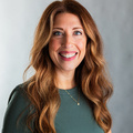 A white woman with red hair, standing in front of a gray background.